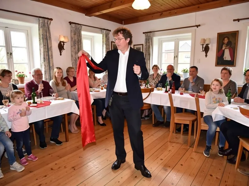 Tryllekunstner trækker et langt rødt silketørklæde frem foran børn og voksne ved festbordene