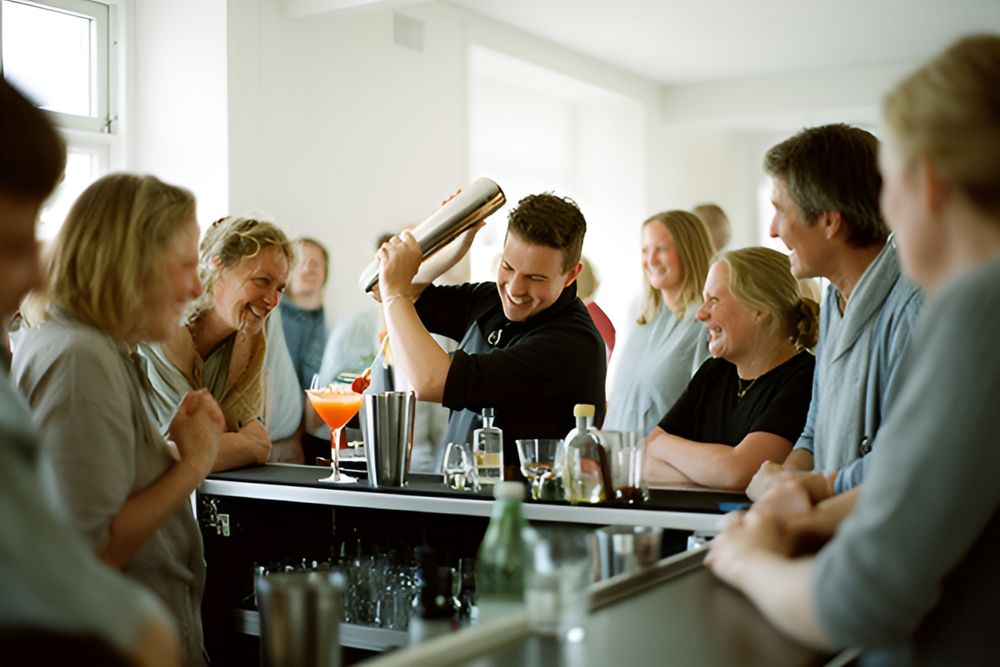 Bartender ryster en cocktail ved en bar, mens gæster ser på og smiler