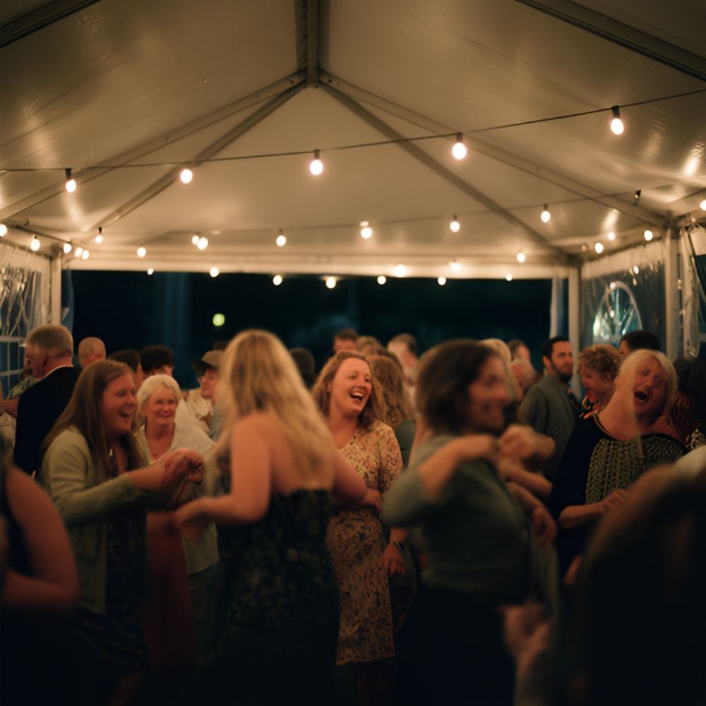 Gæster danser under lyskæder i et festtelt om aftenen