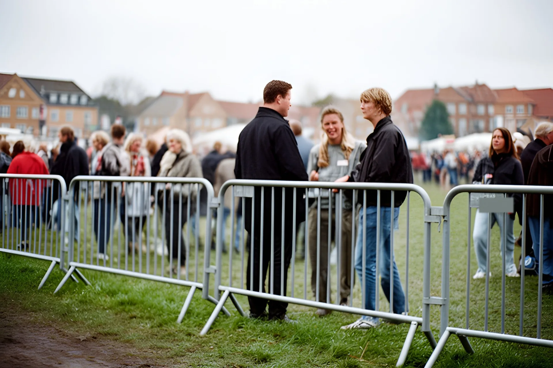 Afspærringshegn på en græsplæne ved en folkefest, gæster står og taler bagved