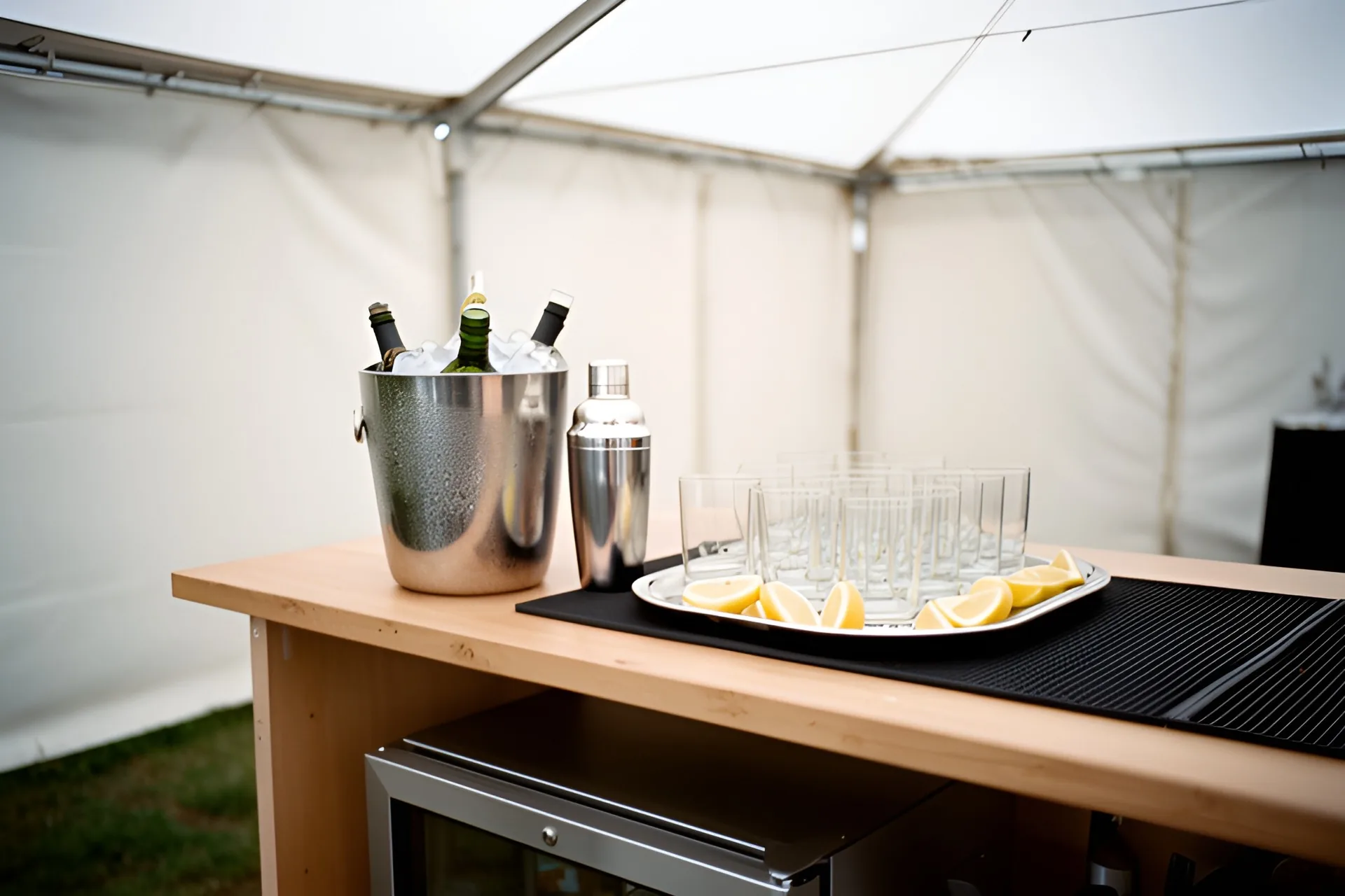 Barbord i et telt med champagnekøler, shaker og en bakke med glas og citronskiver